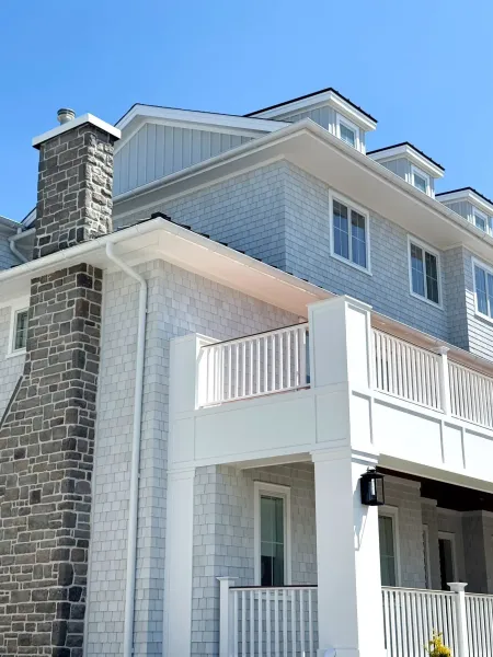 Gray cedar-shake home with stone chimney and white seamless gutters and downspout in Ventnor, NJ