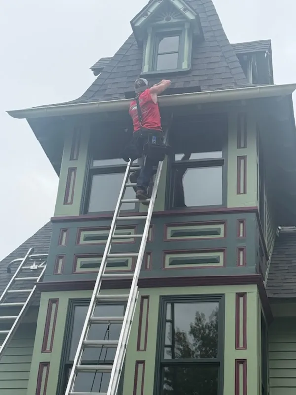 Gutter technician on a ladder at the roofline of a Victorian home in West Berlin, NJ